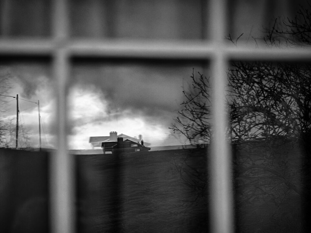 a black and white photo taken through a windowpane with a house in the distance across a field